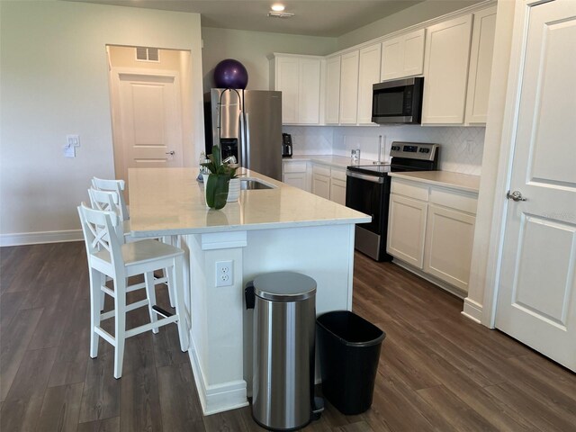 kitchen featuring appliances with stainless steel finishes, white cabinets, decorative backsplash, a kitchen island with sink, and dark wood-type flooring