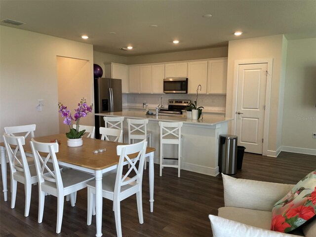 kitchen featuring an island with sink, appliances with stainless steel finishes, dark wood-type flooring, and white cabinets