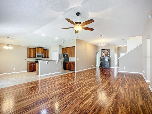 unfurnished living room featuring ceiling fan with notable chandelier, light hardwood / wood-style floors, a textured ceiling, and vaulted ceiling