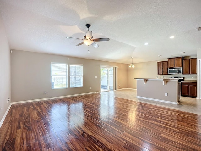 unfurnished living room with ceiling fan with notable chandelier, a textured ceiling, and dark wood-type flooring