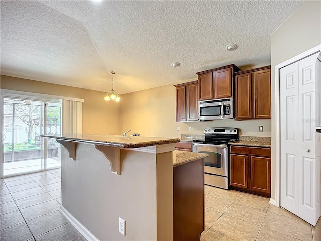 kitchen featuring a breakfast bar, a textured ceiling, stainless steel appliances, a kitchen island with sink, and a chandelier