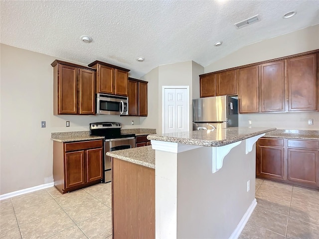 kitchen with light tile patterned floors, stainless steel appliances, a kitchen island with sink, and lofted ceiling