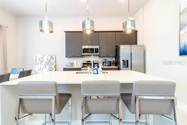 kitchen with decorative light fixtures, stainless steel appliances, a kitchen island with sink, sink, and a breakfast bar