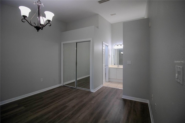 unfurnished bedroom with a closet, a chandelier, hardwood / wood-style flooring, and ensuite bathroom