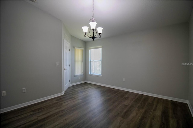 empty room with dark wood-type flooring and a notable chandelier