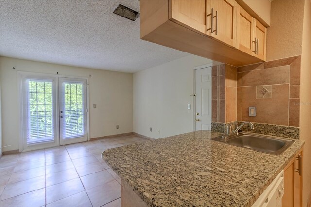 kitchen featuring a textured ceiling, light brown cabinetry, sink, and light tile patterned flooring