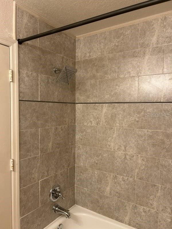 interior details with tiled shower / bath combo and a textured ceiling