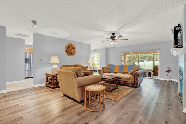 living room with ceiling fan, light wood-type flooring, track lighting, and a textured ceiling