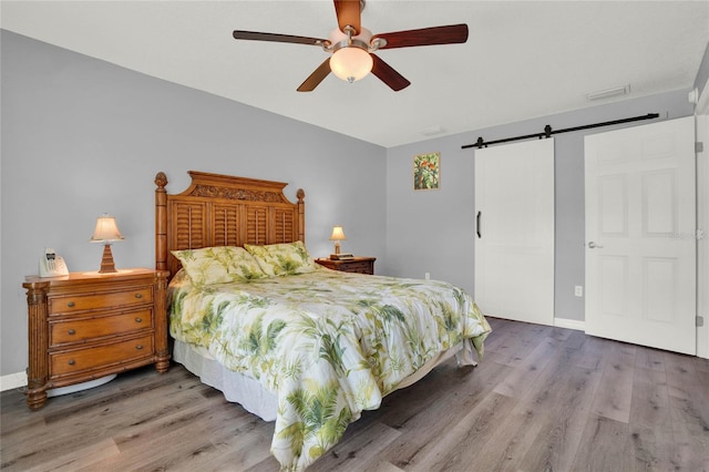 bedroom featuring hardwood / wood-style floors, ceiling fan, and a barn door