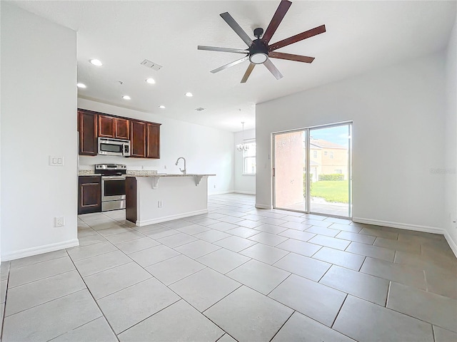 kitchen with light tile patterned floors, appliances with stainless steel finishes, an island with sink, ceiling fan, and a breakfast bar area