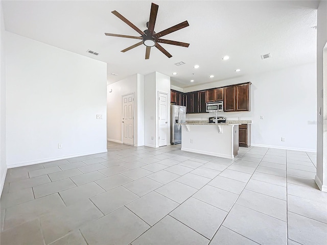 kitchen with a kitchen breakfast bar, a kitchen island with sink, ceiling fan, light tile patterned floors, and stainless steel appliances