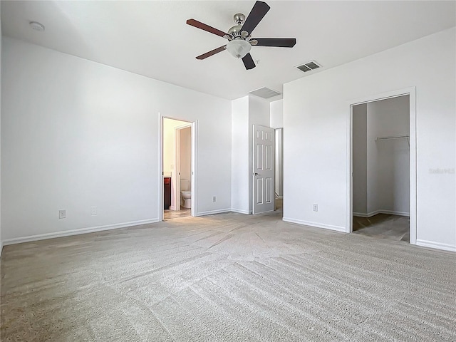 unfurnished bedroom featuring ceiling fan, a spacious closet, light carpet, a closet, and ensuite bath