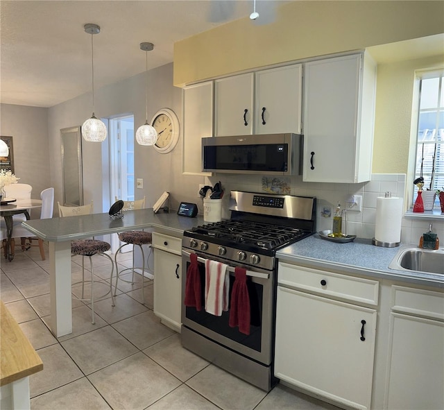 kitchen featuring decorative light fixtures, stainless steel appliances, tasteful backsplash, white cabinets, and light tile floors