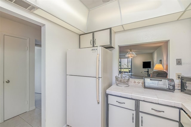 kitchen featuring tile countertops, light tile flooring, white refrigerator, and white cabinetry