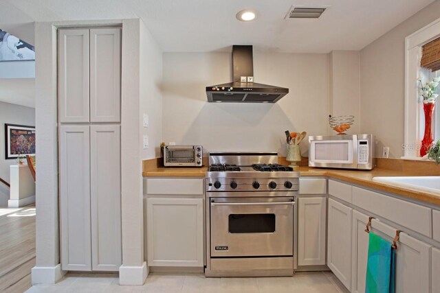 kitchen with stainless steel range, white cabinets, light tile patterned flooring, and exhaust hood