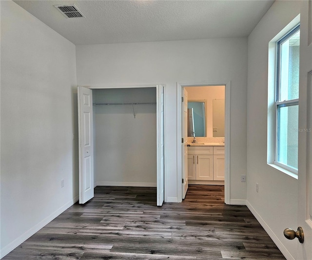 unfurnished bedroom with a closet, connected bathroom, dark hardwood / wood-style floors, and a textured ceiling