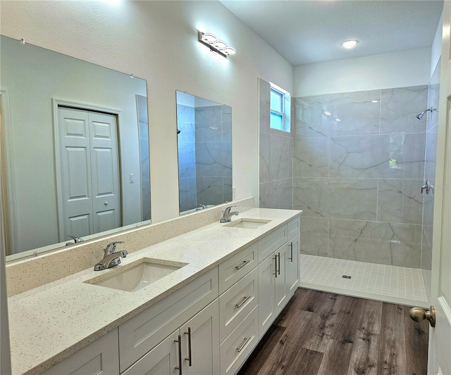 bathroom with dual bowl vanity, tiled shower, and hardwood / wood-style floors