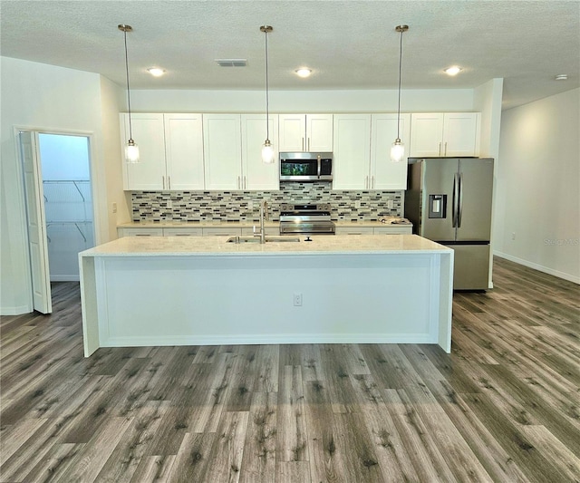 kitchen featuring appliances with stainless steel finishes, a center island with sink, hardwood / wood-style flooring, and hanging light fixtures