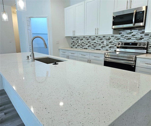 kitchen with pendant lighting, appliances with stainless steel finishes, sink, light stone counters, and tasteful backsplash