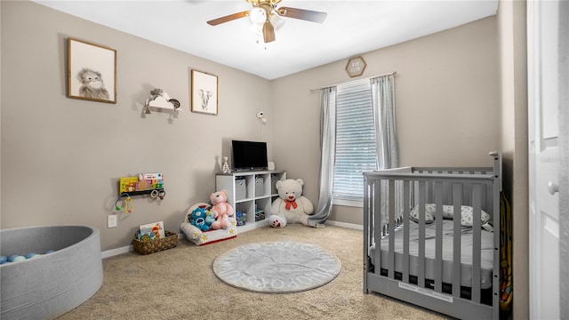 carpeted bedroom with a crib and ceiling fan