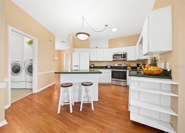 kitchen featuring light hardwood / wood-style flooring, a breakfast bar, washer and clothes dryer, white cabinetry, and appliances with stainless steel finishes