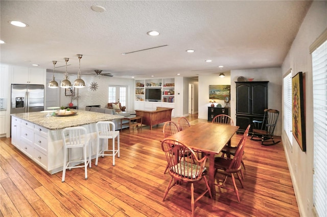 dining room with built in shelves, ceiling fan, light hardwood / wood-style flooring, and a textured ceiling