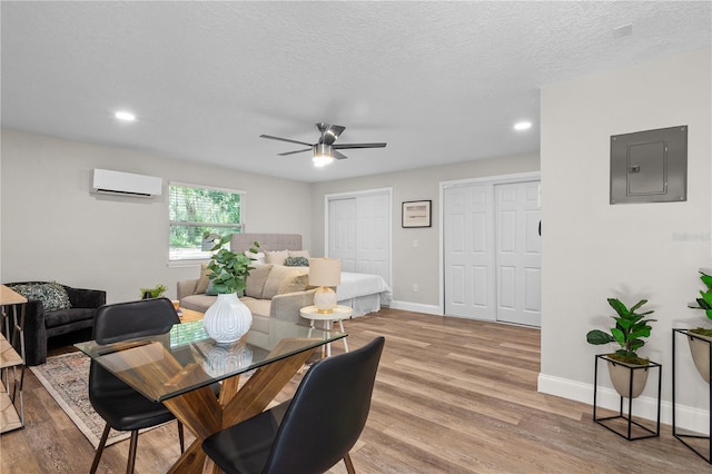 dining space featuring a textured ceiling, light wood-style flooring, baseboards, a wall mounted AC, and electric panel