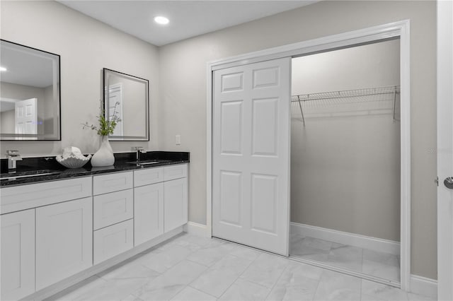 full bath featuring double vanity, marble finish floor, baseboards, and a sink