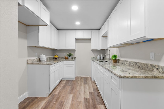 kitchen with light stone counters, recessed lighting, a sink, white cabinets, and light wood finished floors