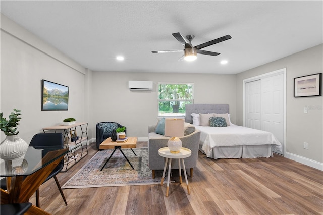 bedroom with baseboards, a wall unit AC, wood finished floors, a closet, and recessed lighting