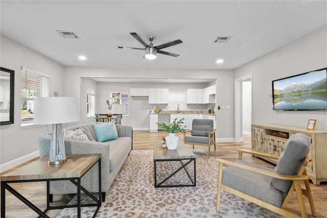 living area featuring light wood-type flooring, plenty of natural light, visible vents, and baseboards