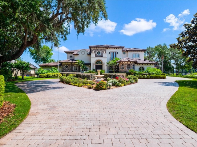 mediterranean / spanish home featuring stone siding, decorative driveway, a tile roof, and stucco siding