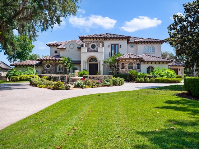 mediterranean / spanish house with driveway, stone siding, a tiled roof, a front lawn, and stucco siding