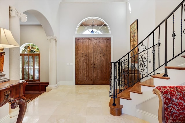 entrance foyer with a healthy amount of sunlight, a towering ceiling, tile floors, and decorative columns