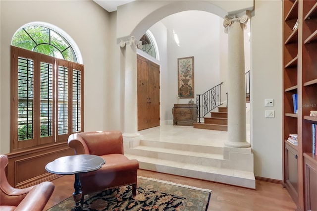 sitting room featuring wood-type flooring, a towering ceiling, and decorative columns