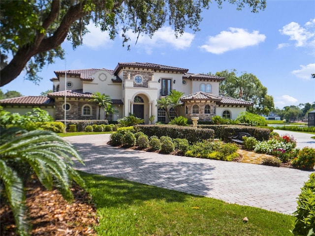 mediterranean / spanish home featuring stone siding, a tiled roof, and stucco siding