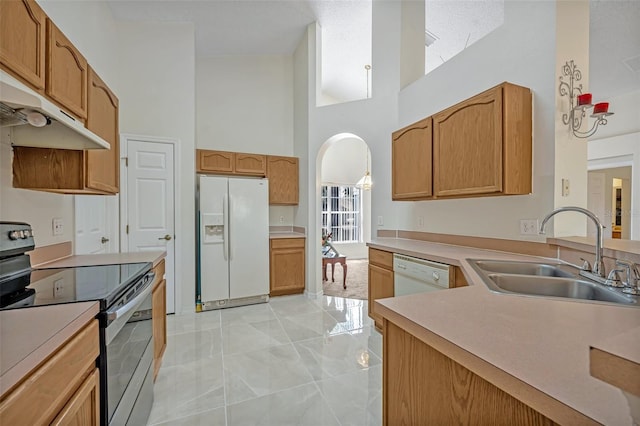 kitchen with sink, white appliances, and a towering ceiling