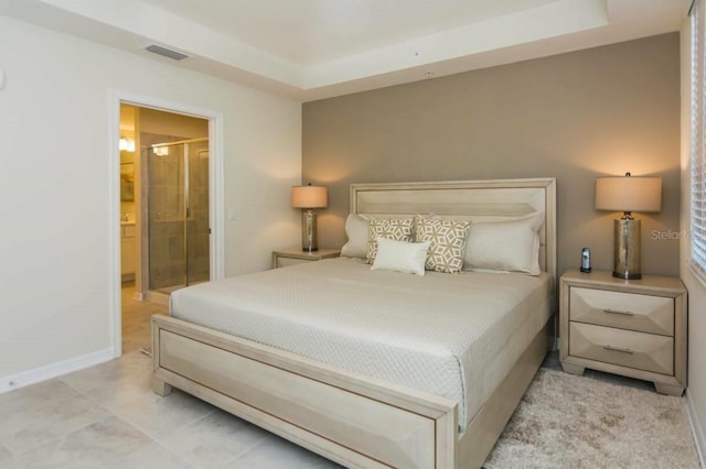 bedroom featuring connected bathroom, light tile floors, and a tray ceiling