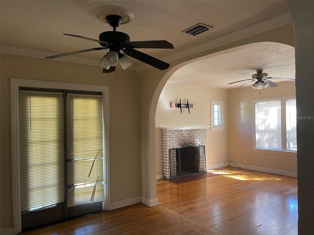 unfurnished living room featuring hardwood / wood-style floors, ceiling fan, a brick fireplace, and crown molding