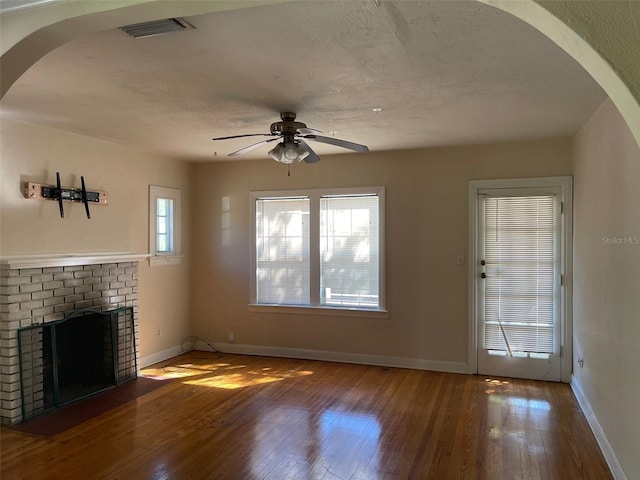 unfurnished living room featuring a healthy amount of sunlight, hardwood / wood-style floors, ceiling fan, and a brick fireplace