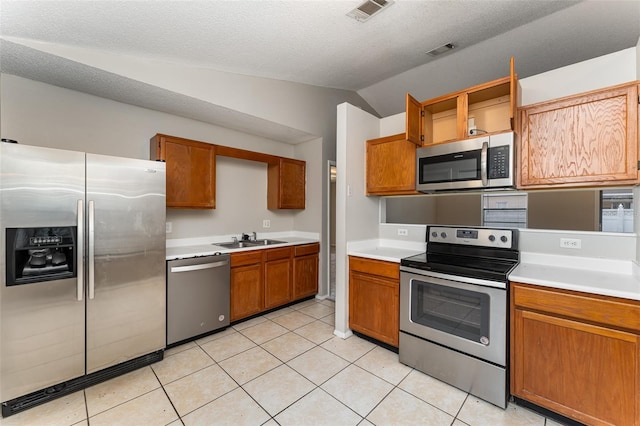 kitchen with a textured ceiling, lofted ceiling, stainless steel appliances, sink, and light tile floors