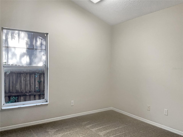 carpeted empty room featuring vaulted ceiling and a textured ceiling