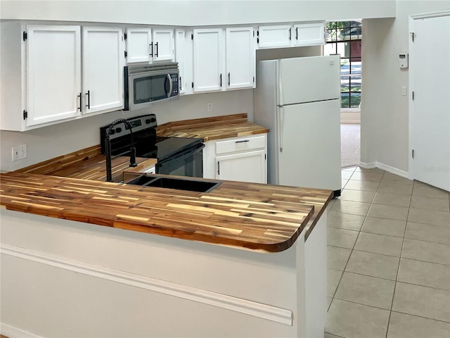 kitchen with kitchen peninsula, stainless steel appliances, white cabinetry, wood counters, and light tile floors