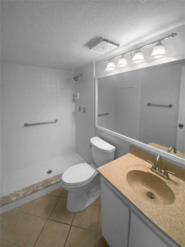 bathroom with vanity, tile flooring, a tile shower, toilet, and a textured ceiling