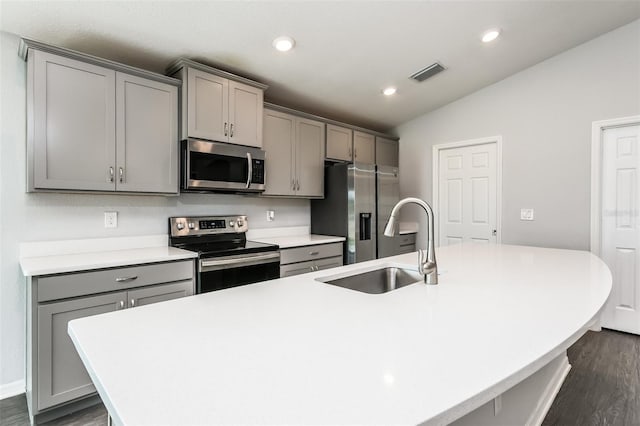 kitchen with gray cabinetry, dark wood-type flooring, appliances with stainless steel finishes, vaulted ceiling, and an island with sink