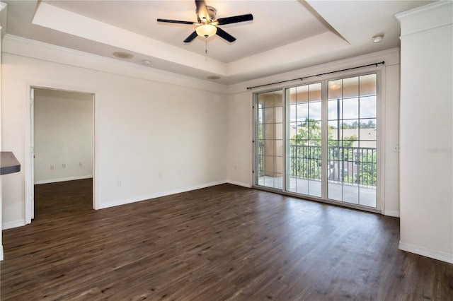 empty room with dark hardwood / wood-style flooring, ceiling fan, ornamental molding, and a tray ceiling