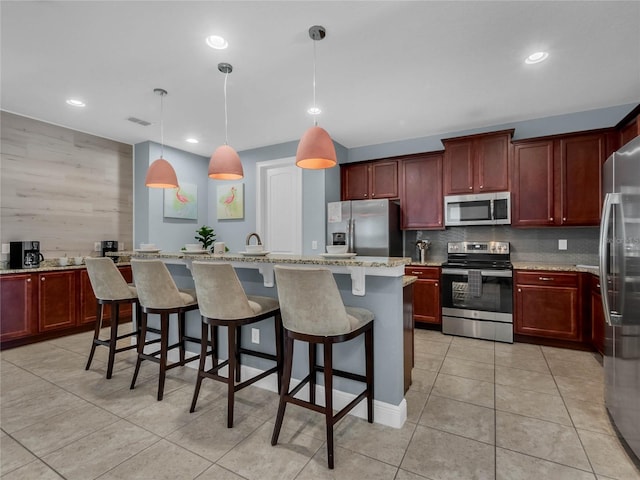 kitchen featuring a center island, decorative light fixtures, light tile flooring, appliances with stainless steel finishes, and a breakfast bar area