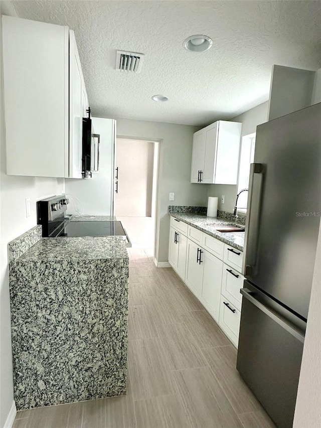 kitchen featuring light stone countertops, white cabinetry, stainless steel fridge, range, and sink