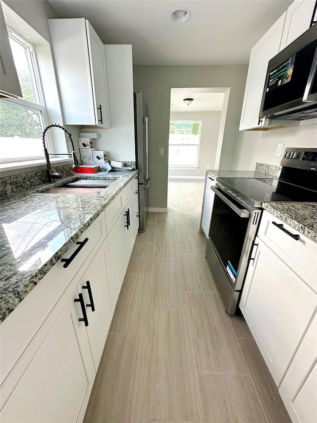 kitchen with white cabinets, light stone countertops, stainless steel appliances, light tile floors, and sink