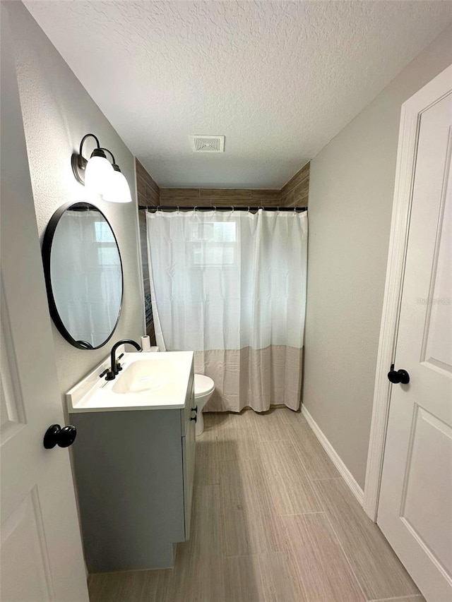 bathroom with a textured ceiling, vanity, and toilet